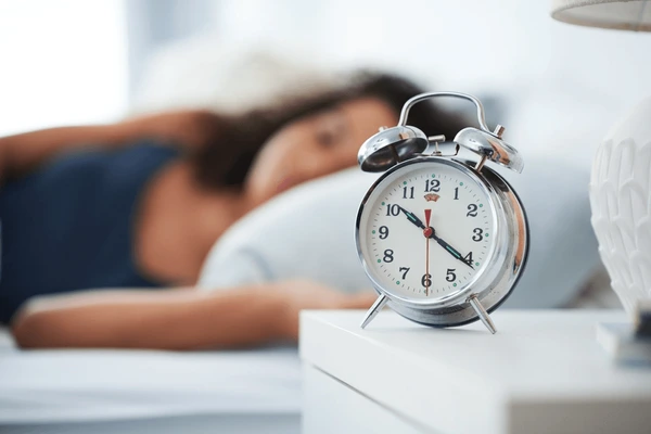 Alarm clock on a nightstand next to a cozy bed during winter.