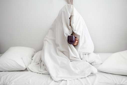 Person journaling their morning routine with a steaming cup of tea from the bed.